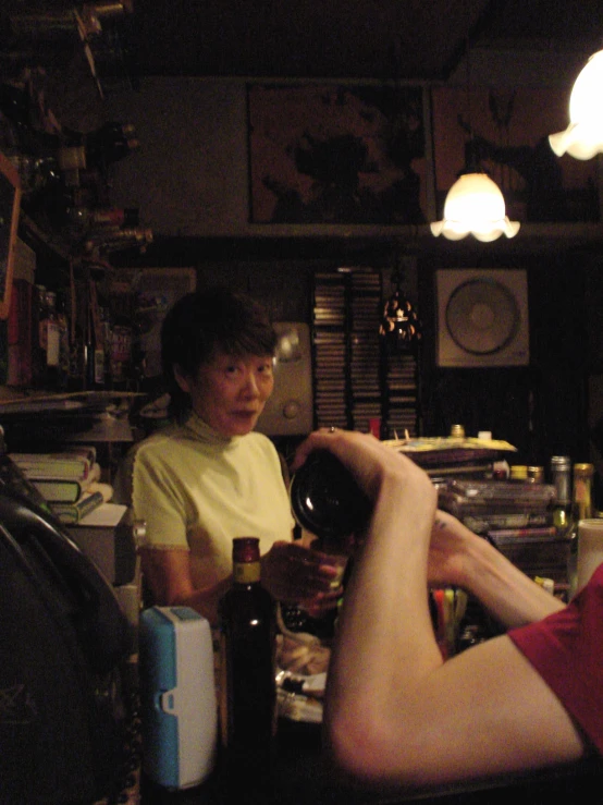 a person wearing a yellow shirt is holding wine bottle in a room with several objects on the wall