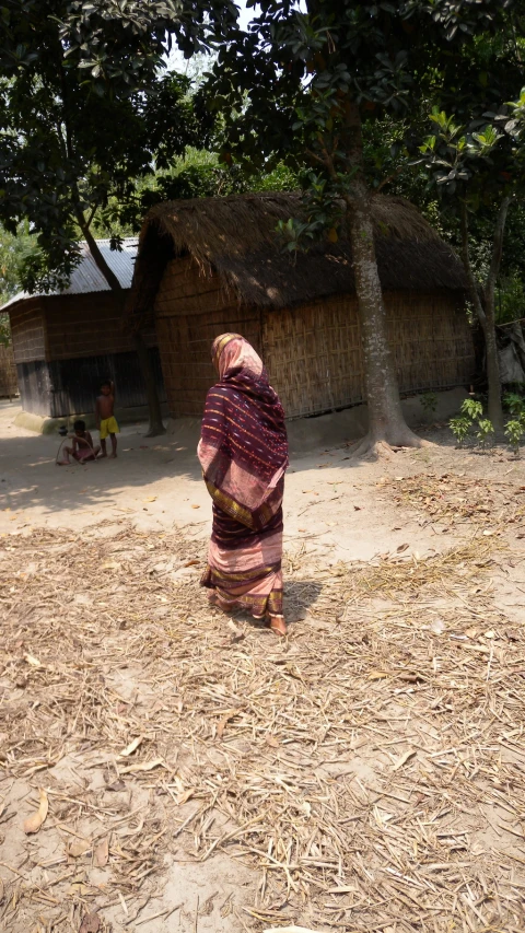 a woman in traditional attire walking in front of a hut