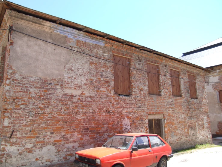 a small orange car is parked in front of a brick building