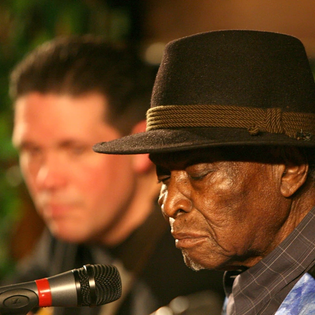 a man in black hat and a microphone and another man wearing blue shirts