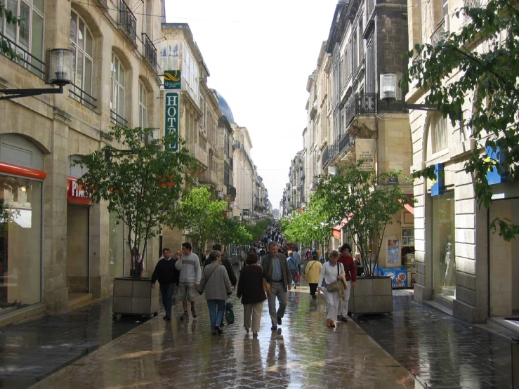 many people walk down a sidewalk between two buildings
