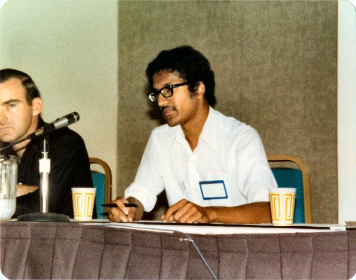 two men sitting at a table with beers and a microphone