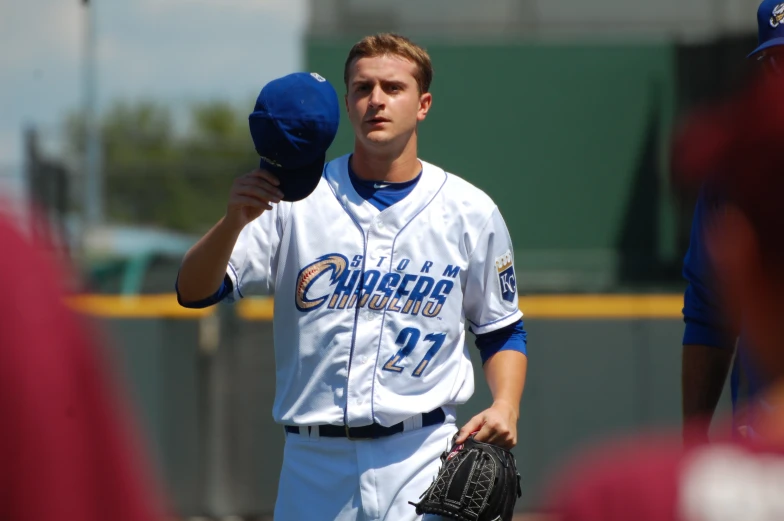 a baseball player wearing a white shirt is holding a hat