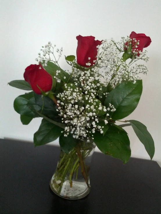 a vase with some red roses and white flowers on a table