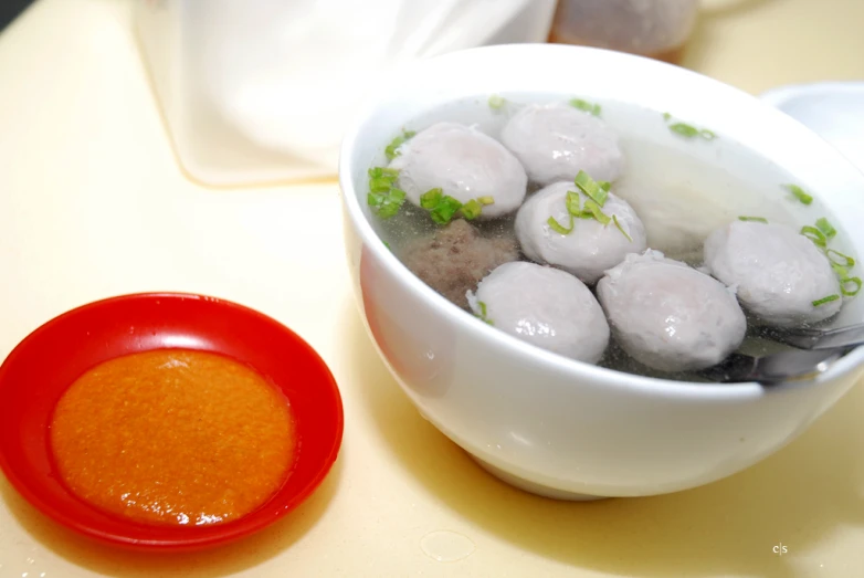 a bowl of soup is next to an orange bowl with meatballs