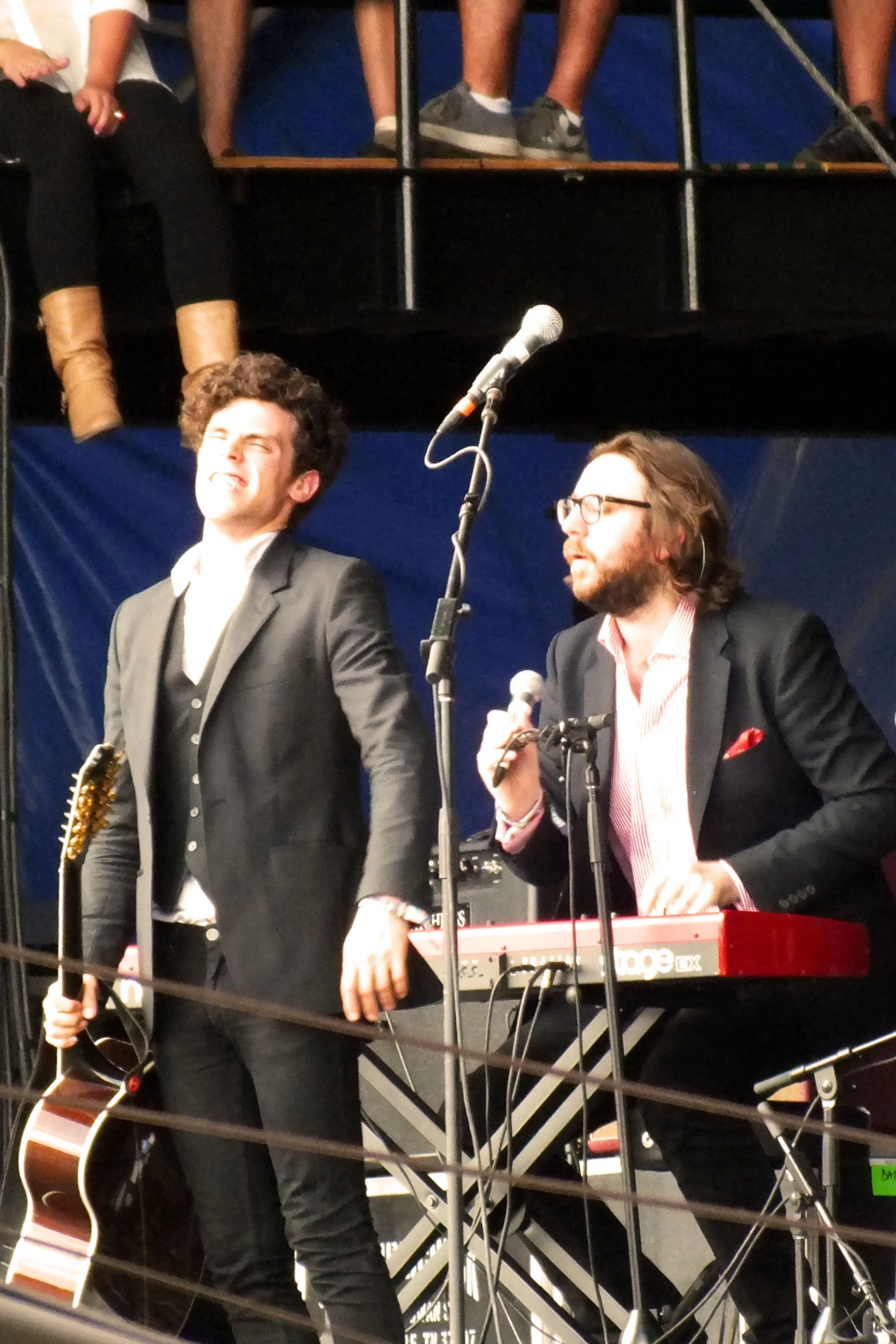 two men with glasses sing into microphones while standing behind a speaker