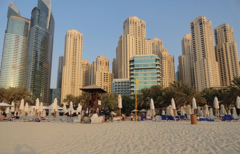 the beach in front of tall buildings is lined with umbrellas