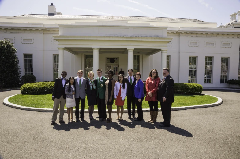 a group of people posing in front of a big house