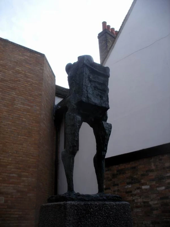 statue of a man with his back turned holding a box outside a building