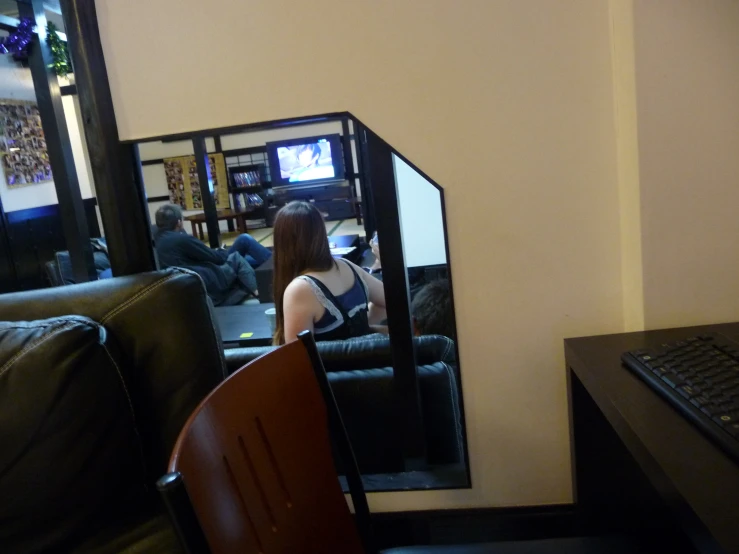 a person sits on a black couch while the reflection of another person's