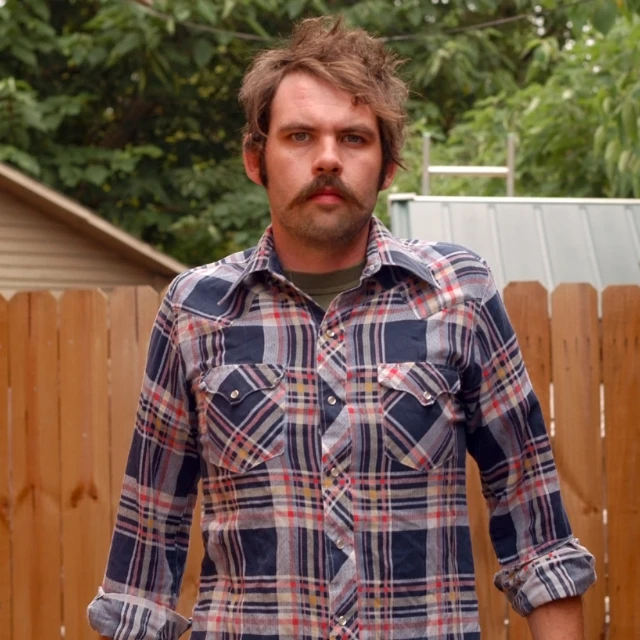 man with mustache and blue and red shirt looking ahead