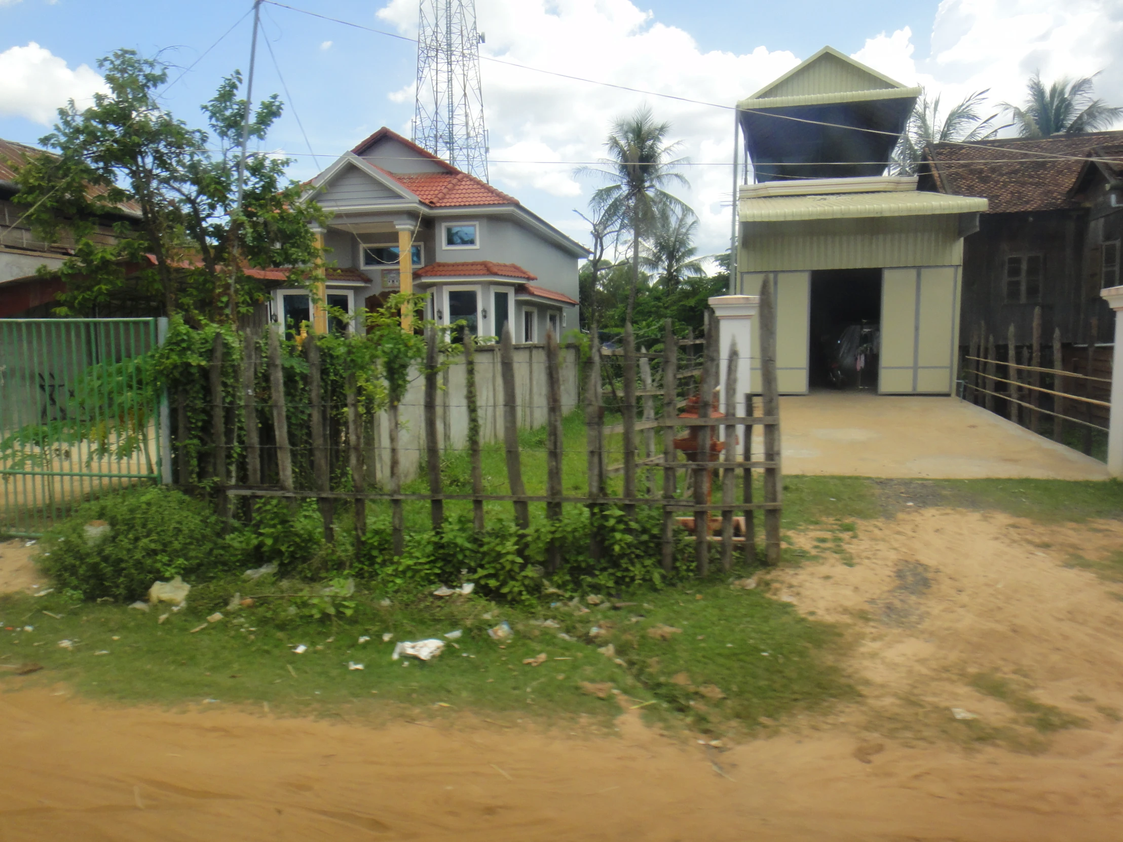 a house behind a fence with weeds growing on it