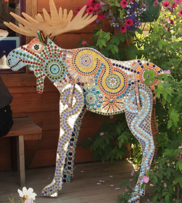 a colorful, mosaic - coated dog next to flowers and a wooden bench