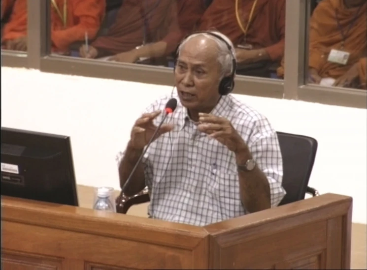 man wearing headphones speaks into microphone at podium