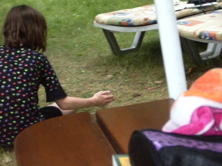 a child sitting down with one hand outstretched at a picnic table