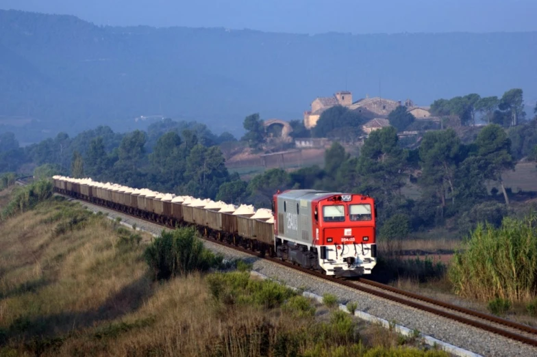 red train moving down the tracks near some mountains