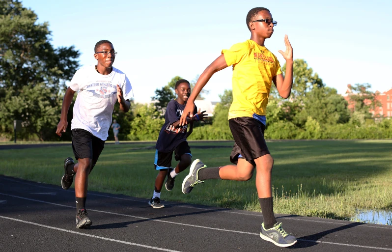 four young men running on a track near trees