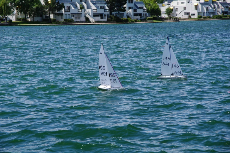 two sail boats are in the water near some houses