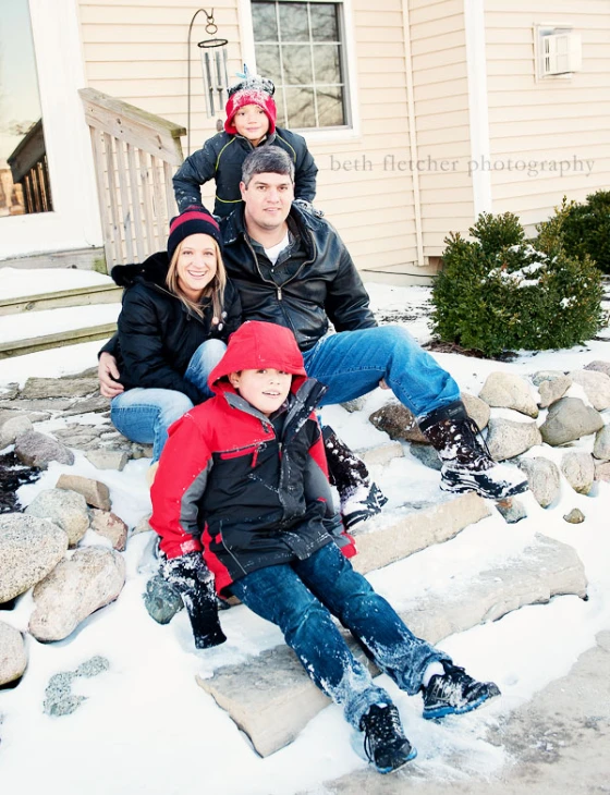 a family sits on steps outside in the snow