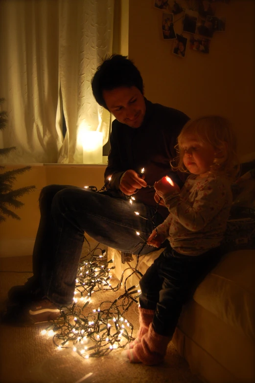 an adult and a small child sitting on the couch with fairy lights in front of them