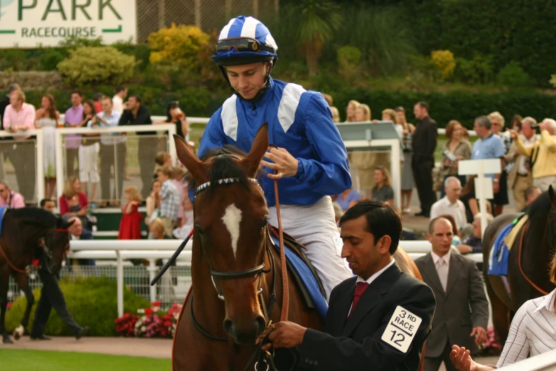 jockey on a brown and white horse, next to a crowd of people