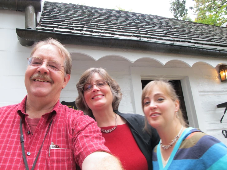 three people pose for the camera outside a white house