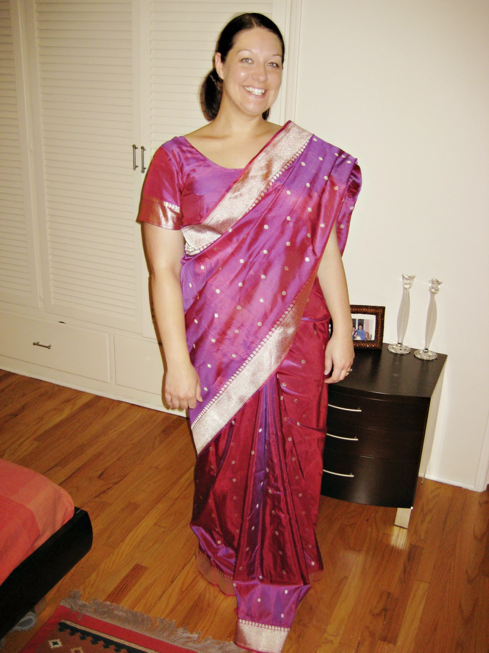 a woman standing wearing a pink saree and smiling