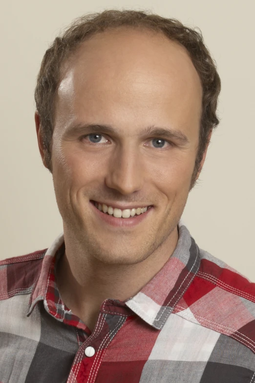 a smiling man in a plaid shirt poses for a portrait