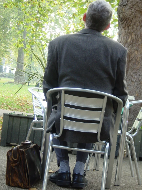 an older man in business attire sitting at a park chair