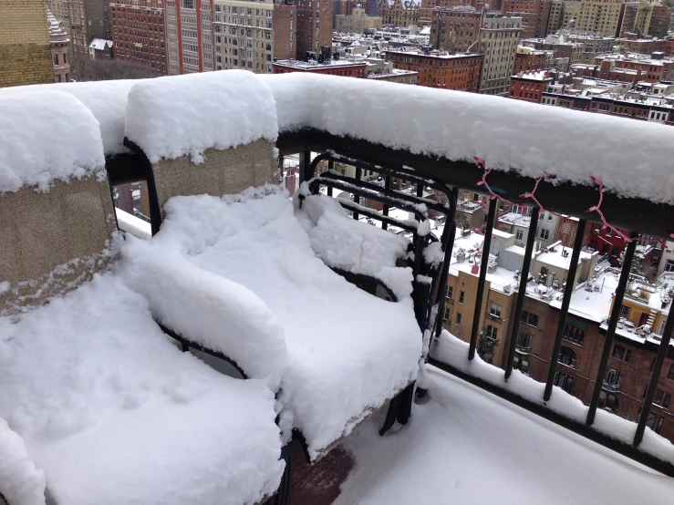 some type of bench is covered with snow in a large city