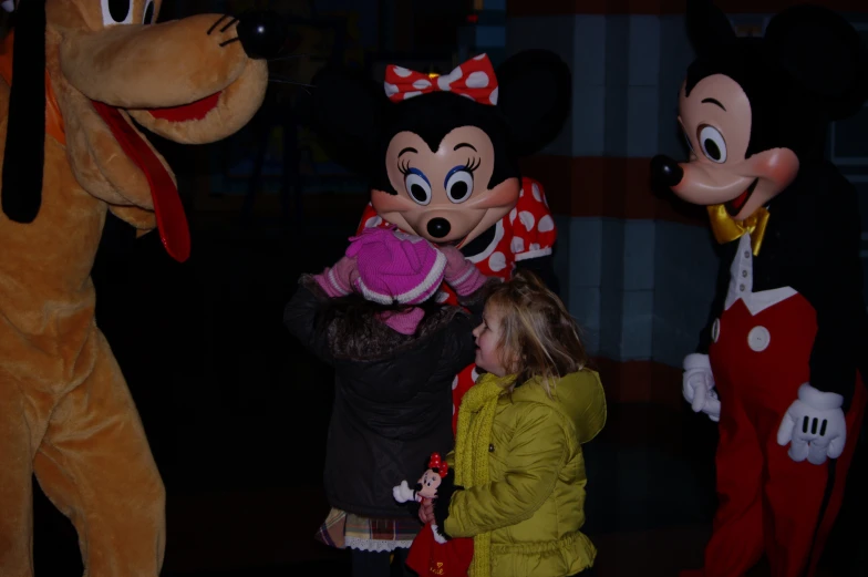 a person holding a stuffed toy while mickey mouse and goofy the frog meet up