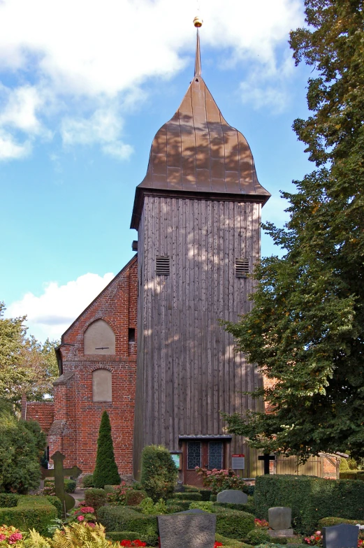 a church with large wooden tower near many small flowers