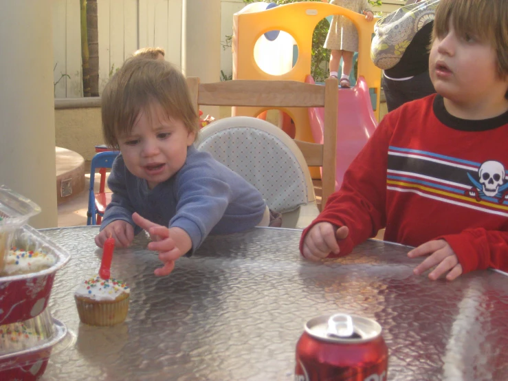 two children at a table eating cupcakes with soda cans