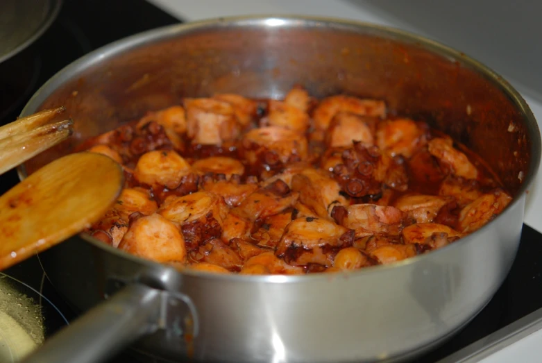 chicken in sauce being stirred in a pot with a wooden spoon