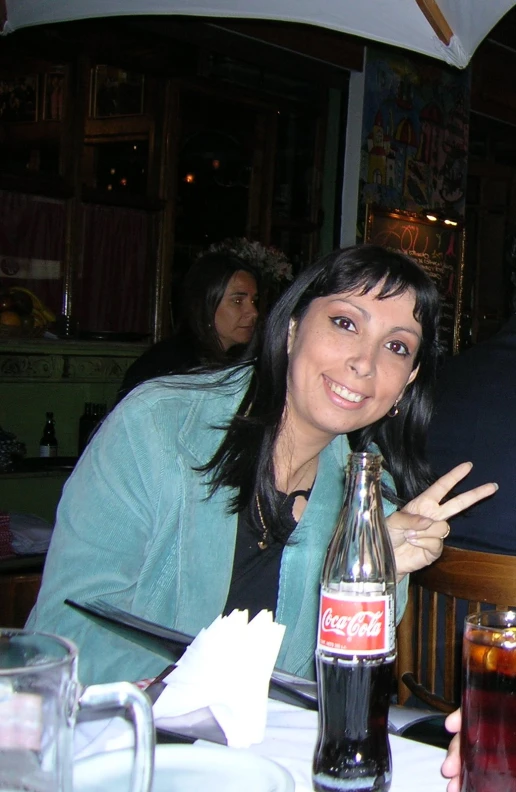 a woman holding up her thumb to the camera and a coca cola bottle