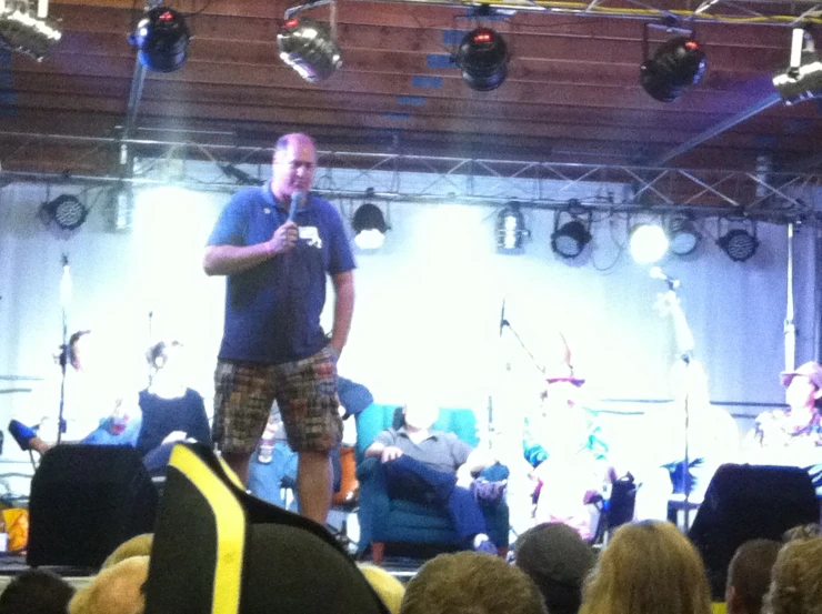 a man in plaid shorts standing on stage holding a microphone