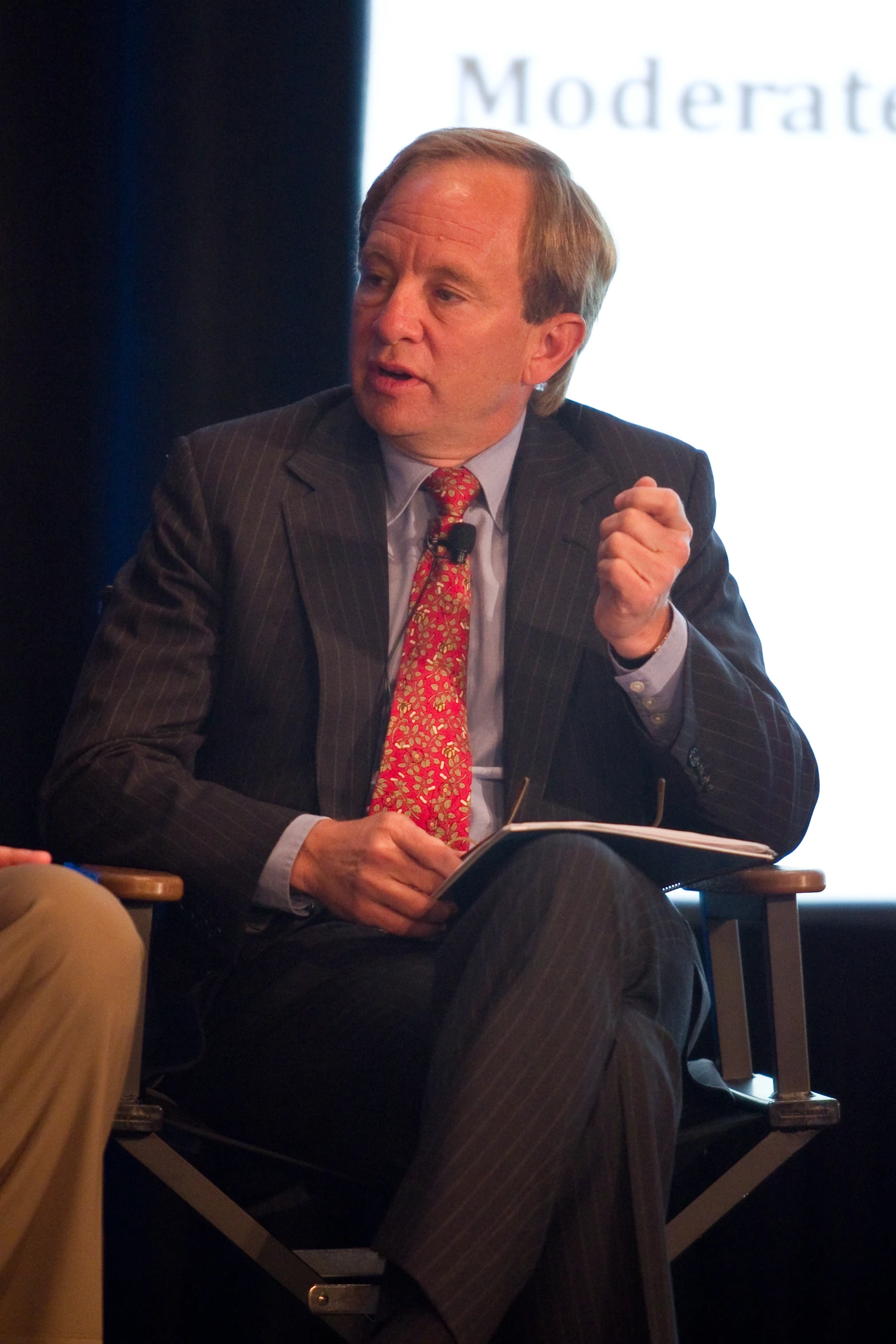 a man with a red tie talking in front of a projection screen