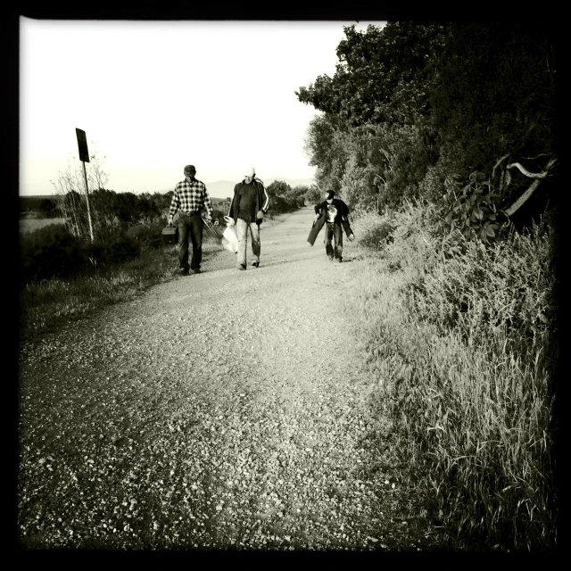 three people crossing a dirt road on a clear day