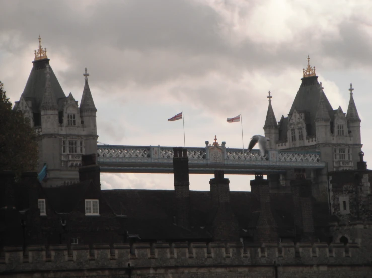 a bridge is in front of two buildings and two towers with flags