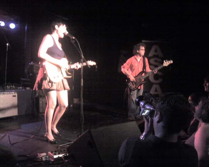 two people on stage one playing guitar and the other singing