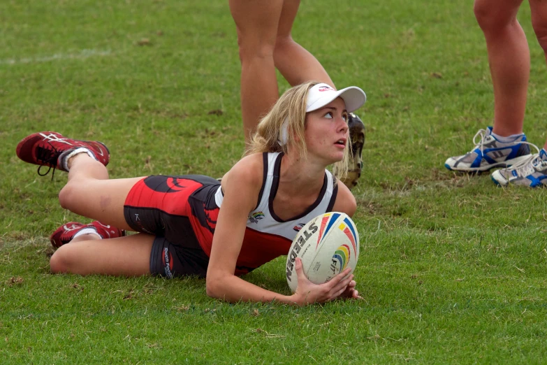 a girl in sports wear laying on grass with a rugby ball