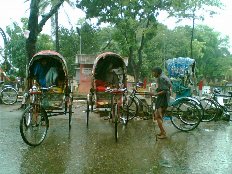 two rickshaws being ridden in the rain by people with umbrellas