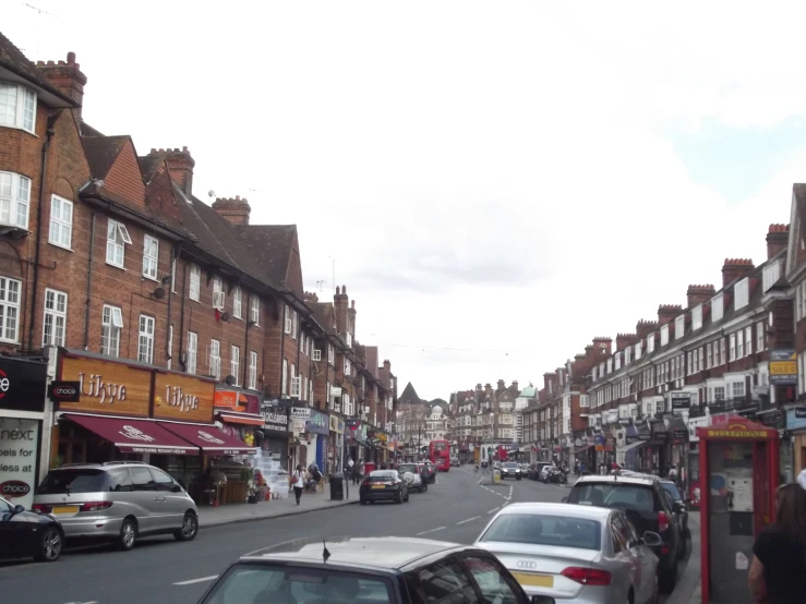 cars and people moving on the street in an area with brown and red buildings