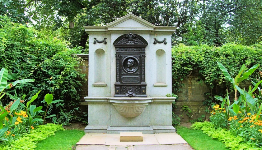 a stone statue sitting on the side of a grass covered garden