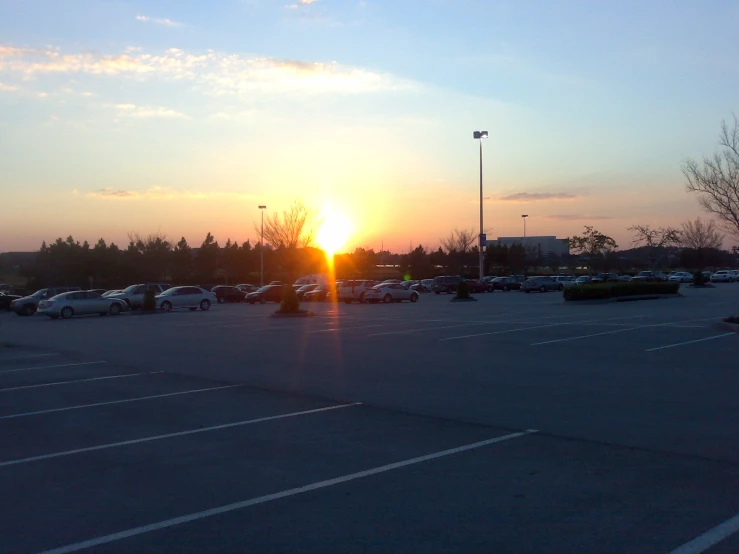 the sun sets in the parking lot as cars are parked