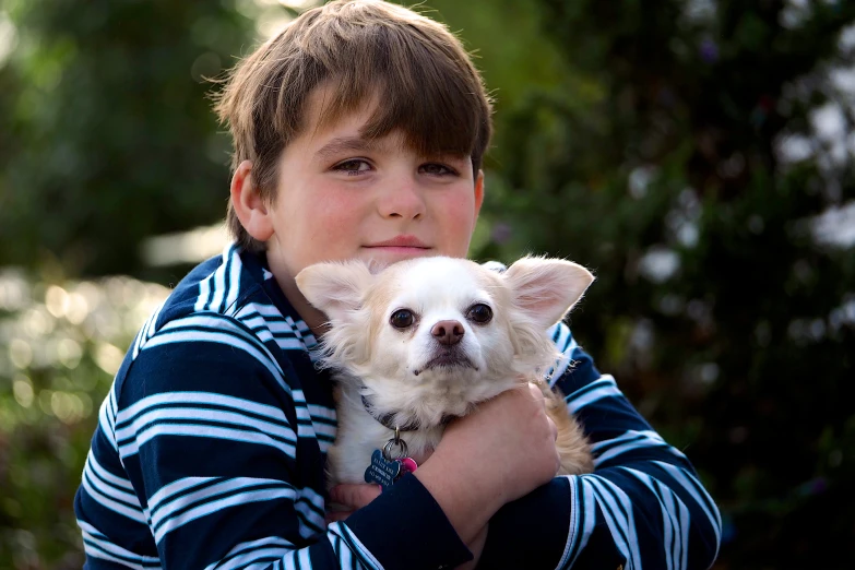 a little boy holding a dog on his arm