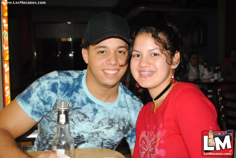 a young man and woman sit at a table in front of a bottle