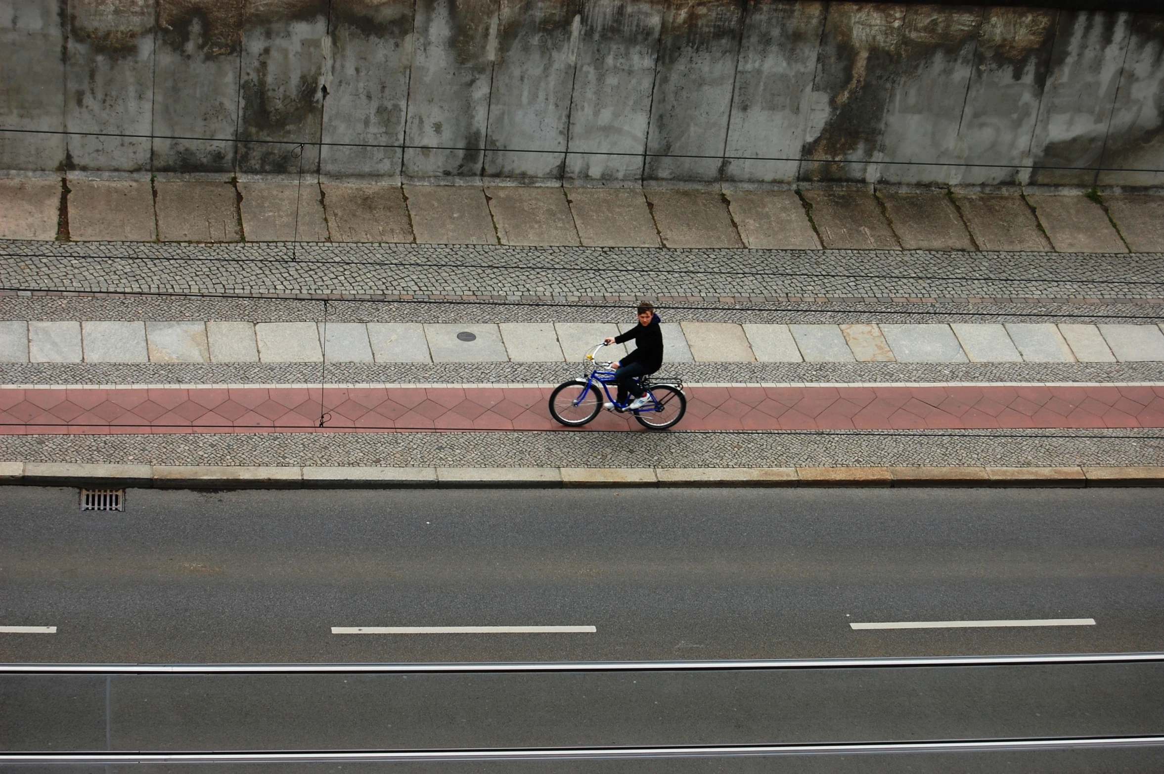 a bicyclist in black is passing a concrete wall