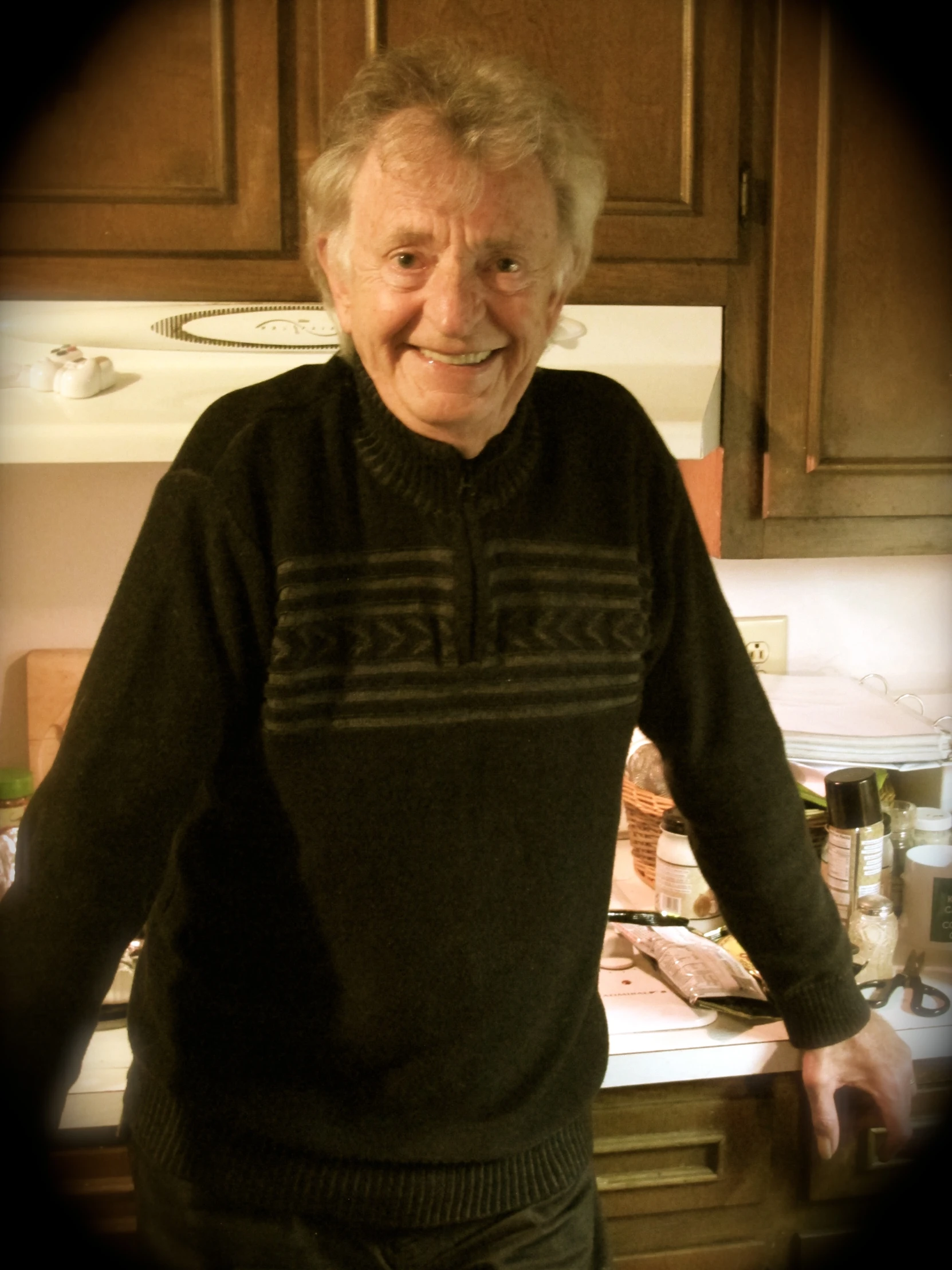 an old man in a kitchen with a microwave in the background