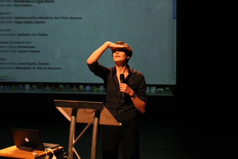 a man is talking in front of a screen with a microphone